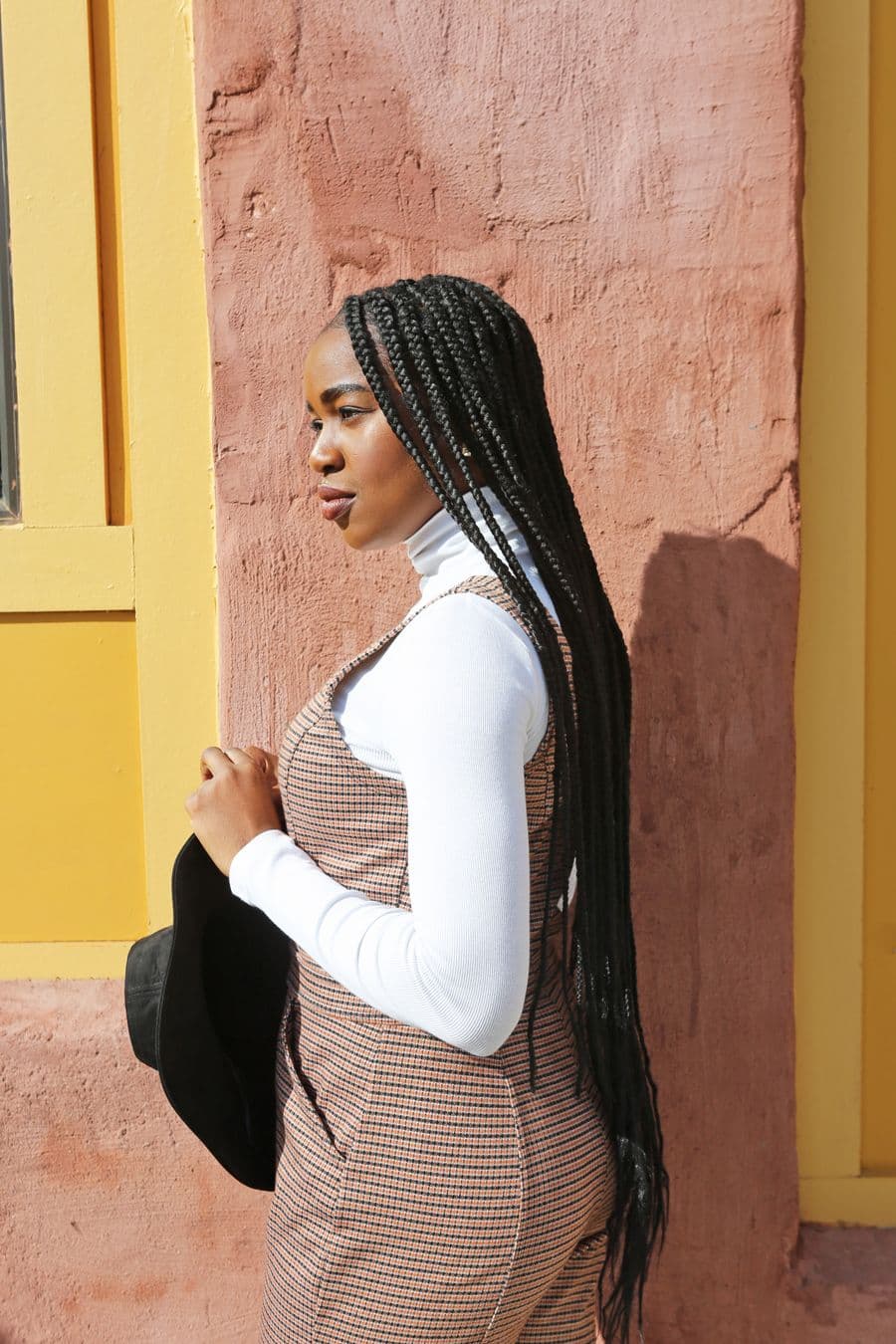 Side profile of long sleek braids against a warm wall